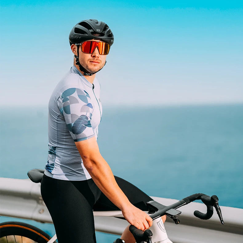 Man with a bicycle on a coastal road with blue sky and ocean in the background